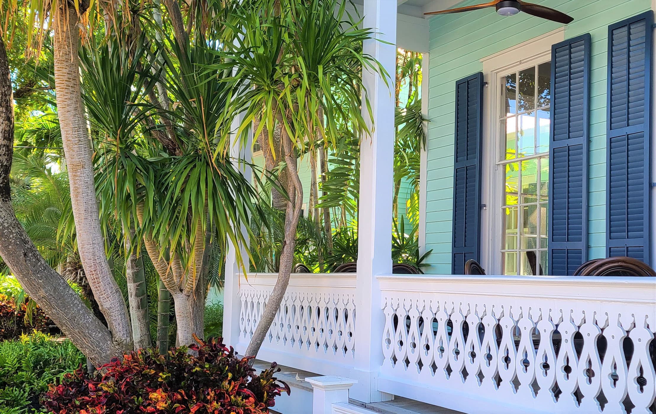 A white porch on a green house with blue shutters
